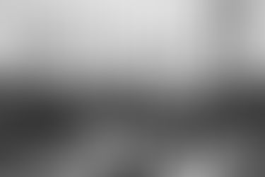 Black and white image of boats with tall masts docked tightly together in a marina during the rain