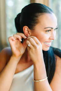 Bride with spray tan putting earring on before wedding ceremony.