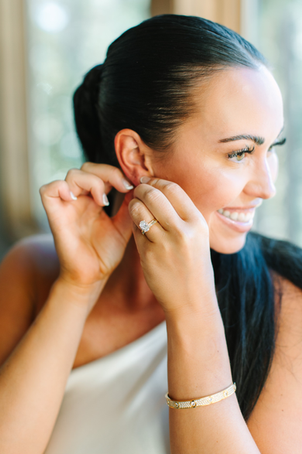 Bride with spray tan putting earring on before wedding ceremony.