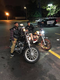 2 members, (wearing cuts) on bikes, in front of cop car