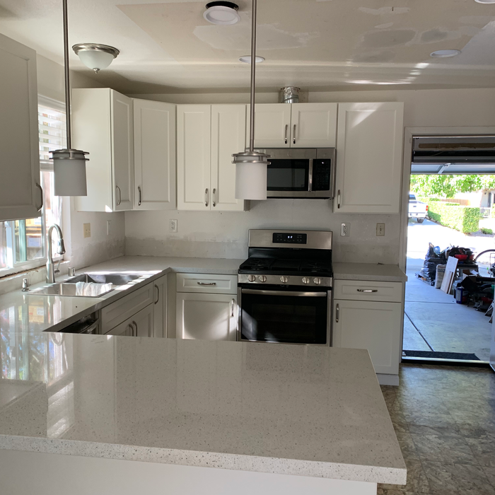 Spacious L-shaped kitchen design with premium white countertops and pendant lighting.
