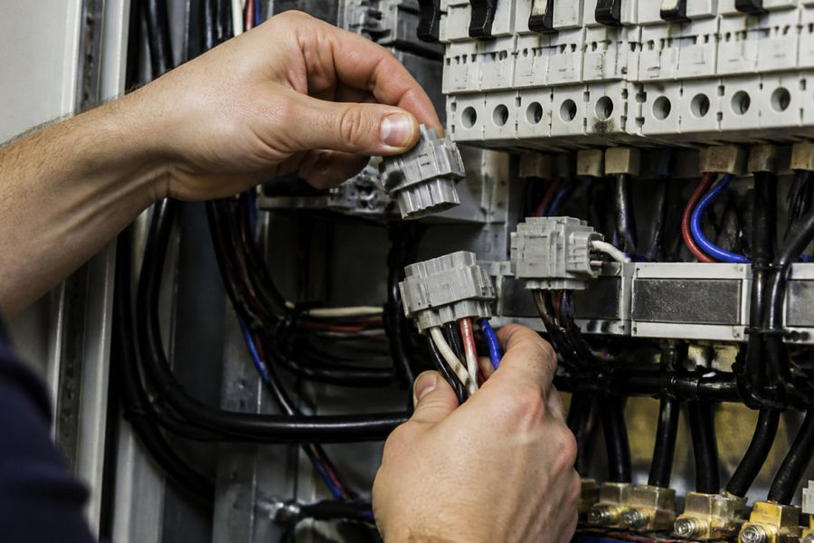 Professional electrician's hands connecting modular power connectors at a retail electrical panel, showing standardized wiring harness connections and circuit breaker adjustment with natural workshop lighting