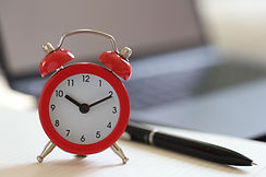 Do less and have more time to earn more, red clock, blurred laptop, black writing pen