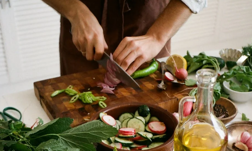 Halal Restaurant, Halal Beef, Halal Meat, Hands chopping vegetables on a wooden board, surrounded by fresh greens and a salad bowl. A bottle of olive oil is in the foreground.