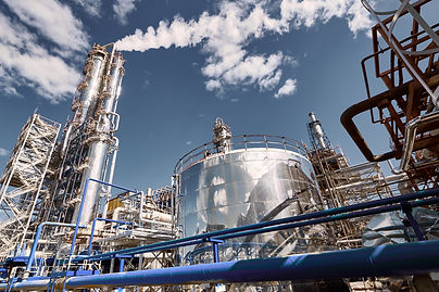 The distillation column at a modern chemical plant under a clear blue sky with steam risin