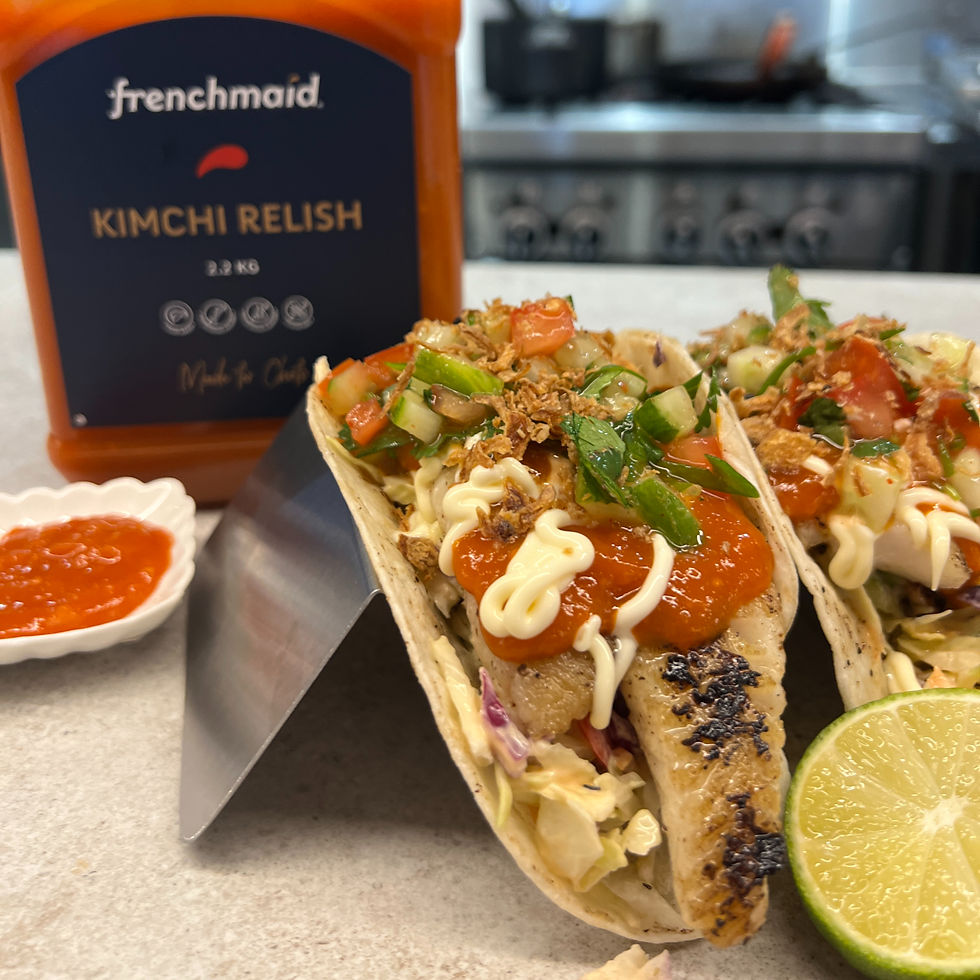Tacos topped with kimchi relish, veggies and sauce beside a Frenchmaid Kimchi Relish bottle and lime in a kitchen.