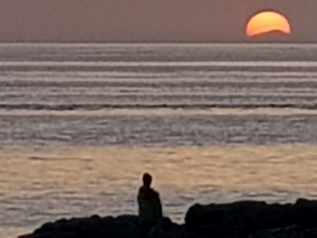 Person sitting on coastal rocks at sunset, reflecting peacefully by the sea, symbolising clarity, self-discovery and the coaching journey.