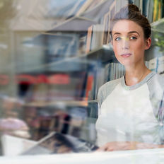 Portrait of a young woman seen through a glass window, with the blurred reflection of the city subtly overlaying her smile.
