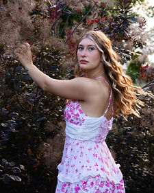 woman in floral dress reaching toward foliage in a stylized cinematic outdoor portrait session