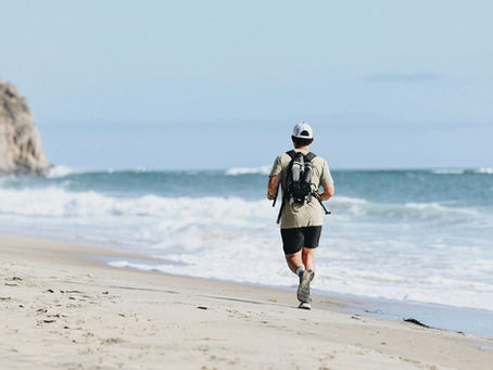 A man running along the beach wearing a backpack.
