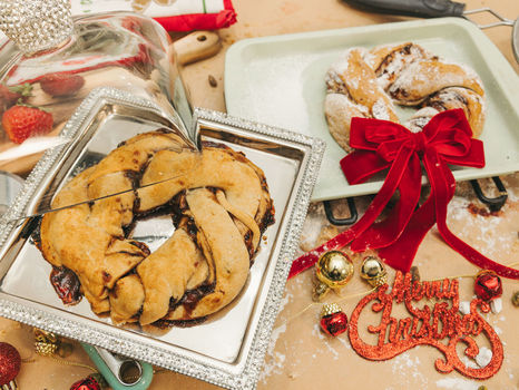 Holiday pastries on trays, one covered, with a red bow and "Merry Christmas" decoration. Strawberries and festive ornaments surround.