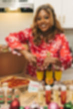 Woman in red pajamas garnishes drinks with cranberries and rosemary. Pizza, festive cocktails, and decorations on table. Joyful holiday scene.