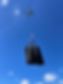 Drone carrying a black bag against a clear blue sky with a few white clouds, conveying a sense of technology and modern logistics.