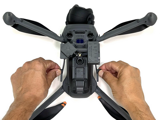 Hands adjusting the arms of a gray drone on a white background. The drone features various markings and textures.