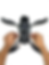 Hands adjust a gray drone on a white background. The drone's arms are spread, with visible text and components underneath.