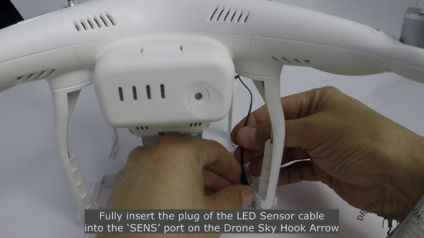 Hands plug an LED sensor cable into a drone's "SENS" port. Text below reads: "Fully insert the plug...Drone Sky Hook Arrow."