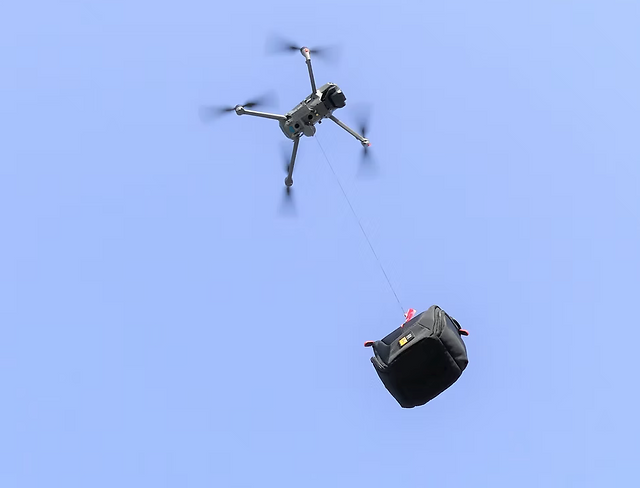 A drone carrying a payload with a hook attached to its bottom