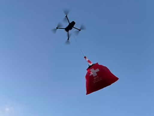 Drone carrying a red bag with a medical cross flies in a clear blue sky. The bag has a small Canadian flag attached.