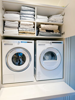 Do It Simpli | A laundry area with stacked washer and dryer units below shelves of neatly folded white towels.