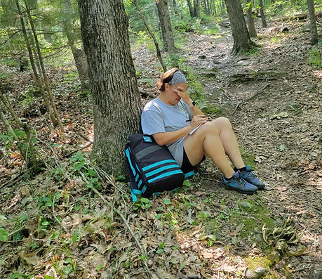 Woman sitting at the base of a tree, covering her eyes while she cries as she reflects during TheraRuck