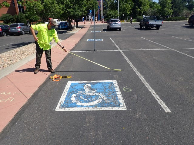 A technician stands to the left of an accessible parking space and pushes out a tape measure across its width.