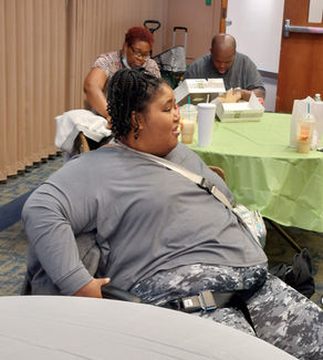 A People On the Go female member with intellectual and/or developmental disabilities listens while sitting at a conference table in the September 2022 Quarterly Meeting. Other members in the background eat lunch.