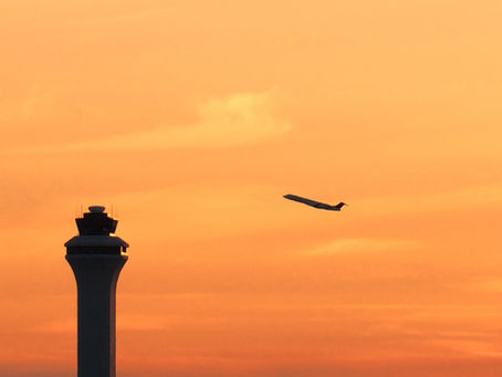 Flughafentower im Vordergrund während im Hintergrund ein Flugzeug auf der Startbahn abhebt