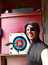 Romulo smiling and wearing a grey hoodie and a black eye patch pointing to a target with arrows