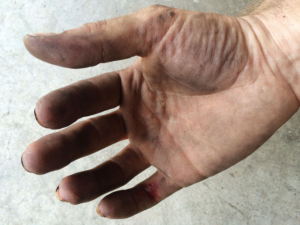 A dirty right hand with a cut on the pinky finger held above concrete in soft but raking light
