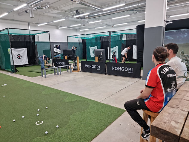 Two people sitting and people playing golf on golf simulators