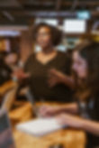 Person speaking and leading a discussion while others take notes at a table