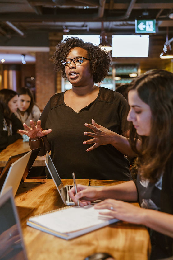 Person speaking and leading a discussion while others take notes at a table