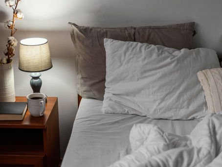 Bett abends, angeknipste Nachttischlampe, Tasse Tee