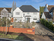 White two-story house with dark roof, flanked by similar houses, in daylight. Red brick fence and small trees in front, under clear blue sky