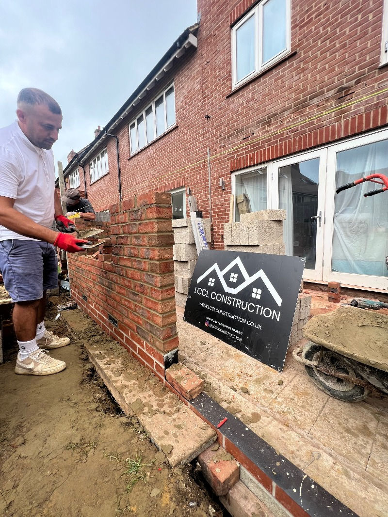 A bricklayer continues work on building red brick walls for the rear house extension