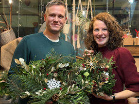 Man and woman smiling, holding festive Christmas wreaths at Island CraftWorks, Ryde, Isle of Wight