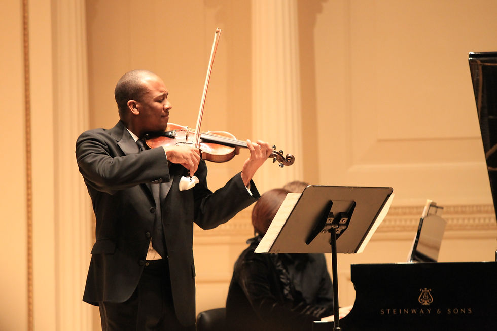 A middle-aged Black man stands in a black suit and play the violin on a stage