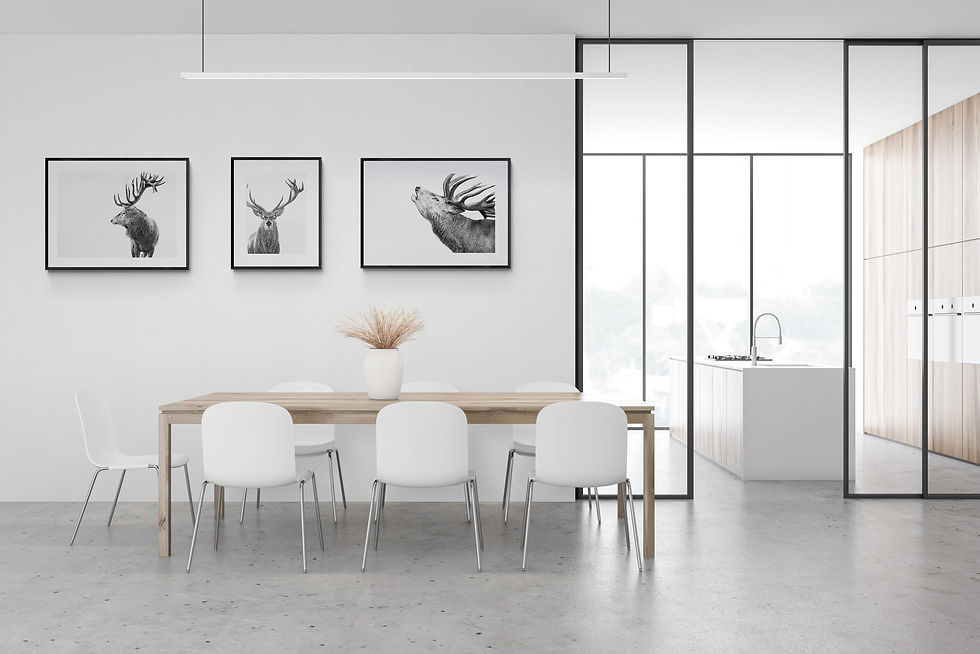 Modern dining room with a wooden table, six white chairs, and a vase of dried grass. Three framed deer art pieces on the wall. Minimalist kitchen in the background.
