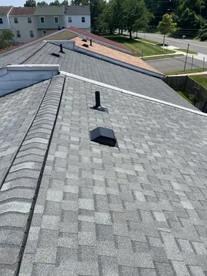 gray-asphalt-shingle-roof-with-vents-and-adjoining-homes-visible-in-sunny-neighborhood-showing-finished-installation-related-to-roofing-warranties-explained