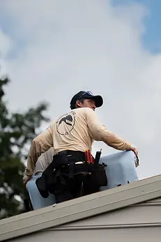 worker-in-tan-shirt-with-restoration-roofing-co-logo-carrying-material-on-roof-wearing-too