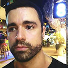 Homem de barba curta, olhando para o lado, em um ambiente noturno com decoração festiva e um número 8 iluminado ao fundo.