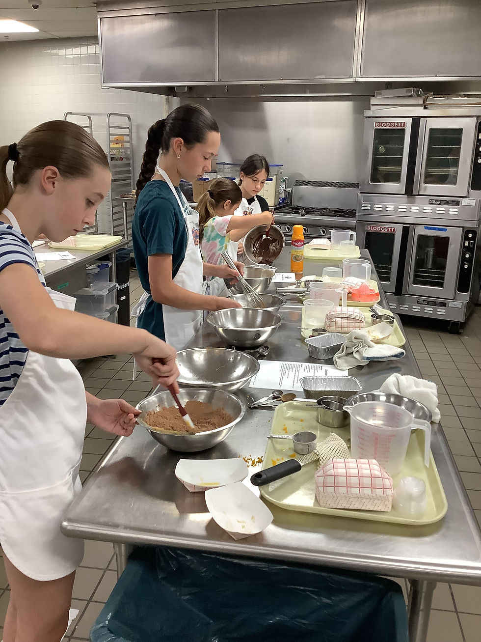 Junior chefs work collaboratively in a professional kitchen, carefully mixing ingredients for their Chocolate Orange Brownies.