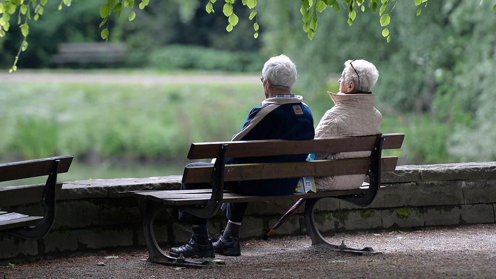 Elderly couple sitting on a park bench looking at a lake
