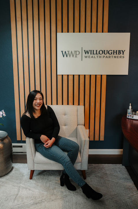 Rizza sitting in a chair in front of a Willoughby Wealth Partners logo and branding by Z Squared Studio on a sign.