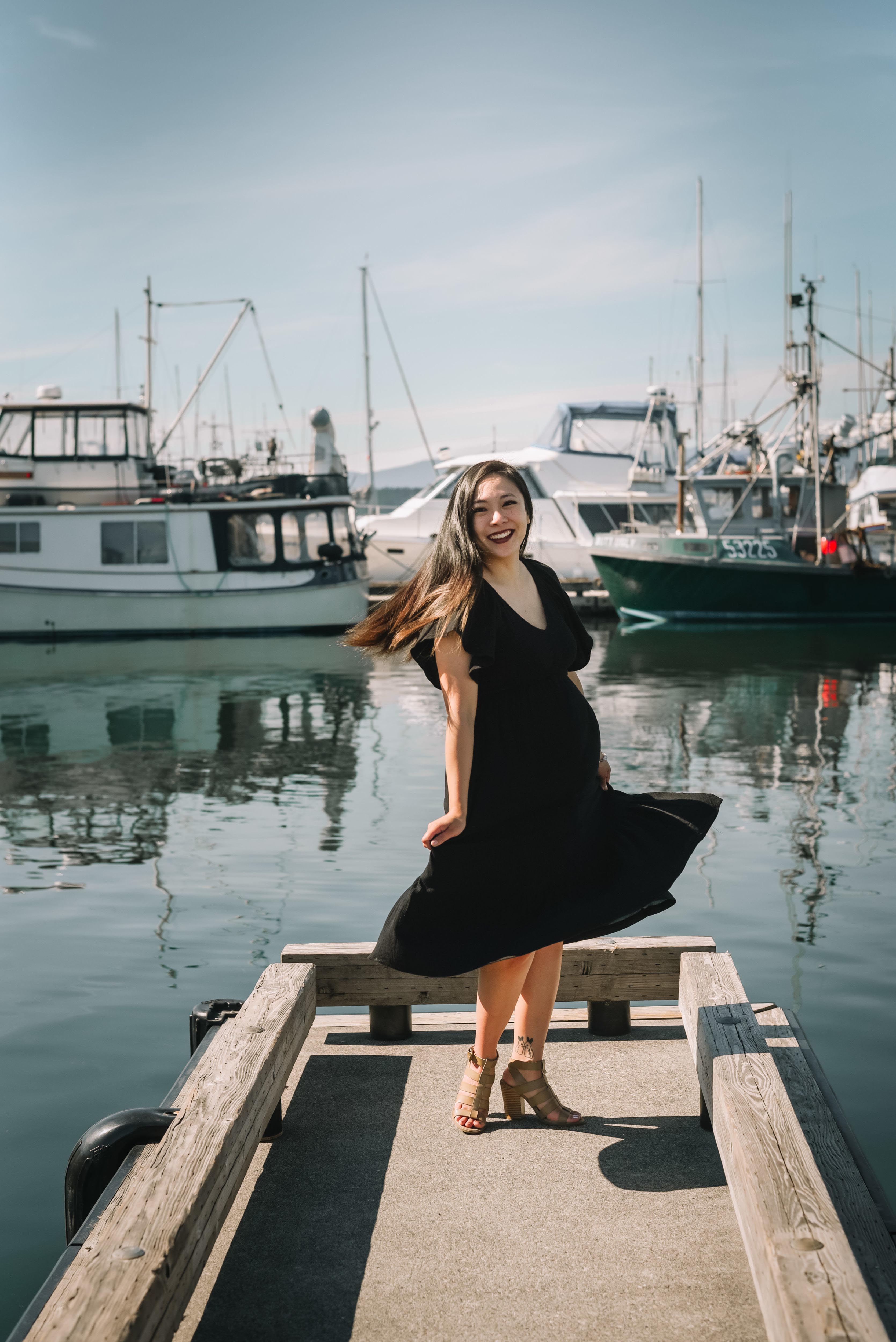 Rizza looking at the camera and spinning on a habor pier with boats in the background.