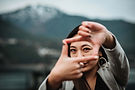 Rizza holding up her hands in a frame and looking through them at the camera, with mountais in the background.