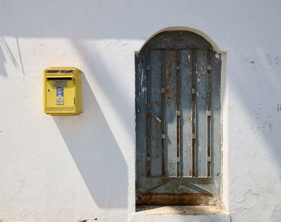 A bright yellow post box beside a grey door in the Sale medina