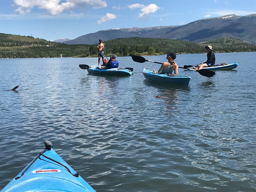 From a kayak, the pictures shows 4 Outdoor Mindset members in kayaks and one paddleboards on the lake.