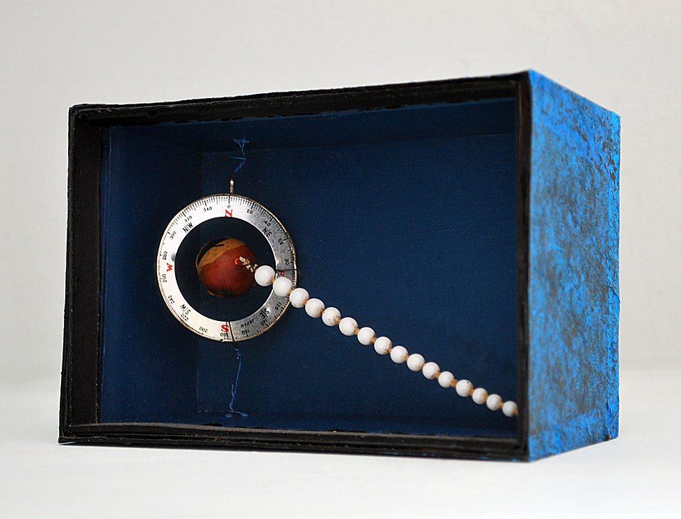 Pulsar by Arthur Bruso. Abstract blue box sculpture with a compass ring marked N, S, E, W and a bead chain stretching across it