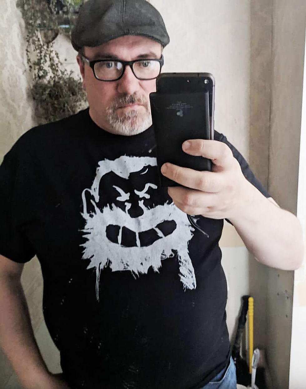 John Zirkelbach wearing a cap and black tee shirt holding an iphone.